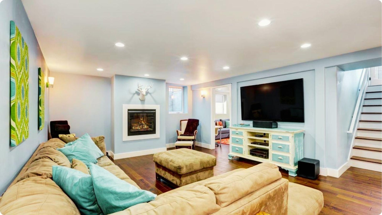 Cozy basement family room with light blue walls, large sectional, fireplace, and mounted TV.